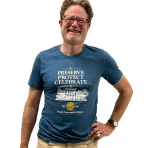 A smiling man wearing glasses and a blue Duluth Preservation Alliance t-shirt that says “PRESERVE PROTECT CELEBRATE.”